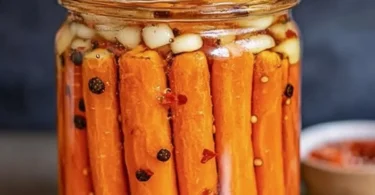 A jar of hot honey pickled carrots with vibrant colors and spices inside.